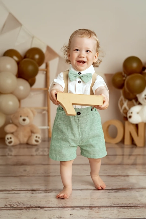 Ein einjähriger Junge hällt lachend die Zahl eins in der Hand bei seinem Fotoshooting zum Einjährigen Geburtstag.
